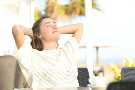 Girl relaxing sitting in a hotel terrace on the beach with arms on headの写真素材