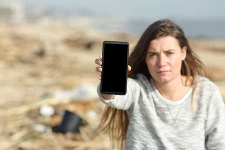 Volunteer showing smart phone blank screen in a dirty beachの写真素材