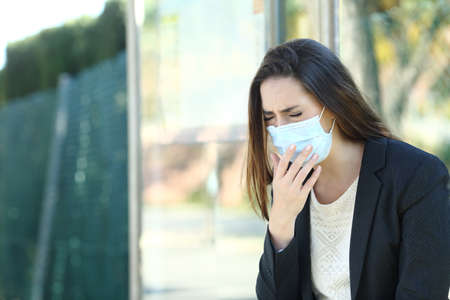 Infected woman wearing a protective mask coughing waiting in a bus stop