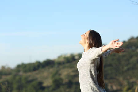 Side view portrait of a happy woman stretching arms breathing fresh air in the mountain