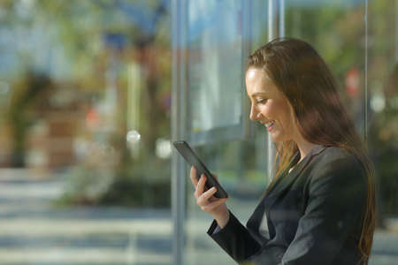 Side view portrait of an executive checking smart phone content waiting in a bus stopの写真素材