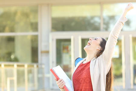 Excited student celebrating good grades raising arms standing in a collegeの写真素材