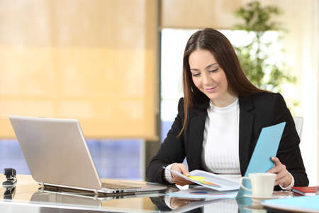 Serious executive checking paper documents sitting at officeの写真素材