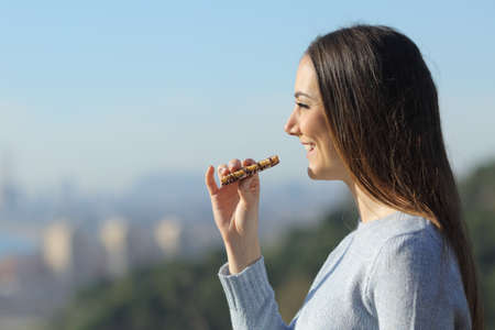 Happy girl eating a snack bar in the city outskirts while contemplating the viewsの写真素材