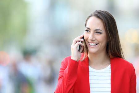 Portrait of a happy woman wearing red jacket talking on the phone looking at side in the streetの写真素材