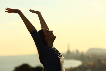 Side view portrait of an excited woman raising arms on a sunset with backlight