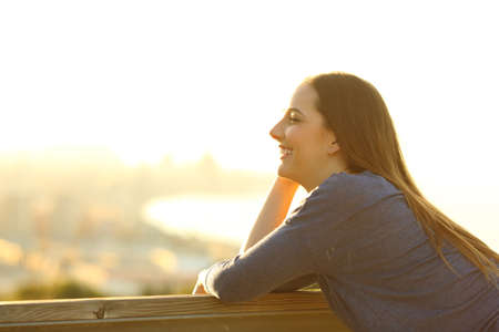 Side view portrait of a happy woman looking away on a sunny terrace with city views at sunsetの写真素材