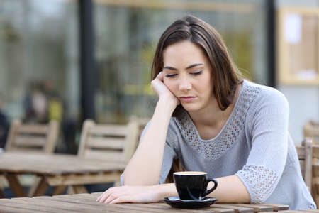 Sad teenage girl looking down pensive on a cafe terraceの写真素材