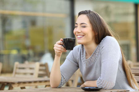 Satisfied happy woman smelling her cup of coffee sitting on a cafe terraceの写真素材