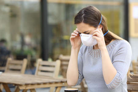 Serious woman putting on protective mask preventing contagion at coffee shop terraceの写真素材