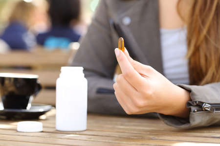 Close up of a woman hand showing supplement vitamin pill on a coffee shop terrace