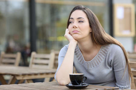 Bored girl looking to the side sitting alone on a restaurant terraceの写真素材