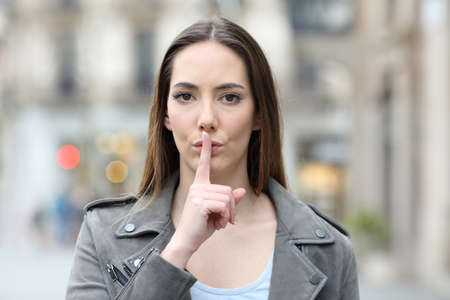 Front view portrait of serious woman asking for silence with finger on lips on city streetの写真素材