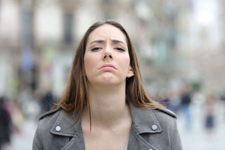 Front view portrait of a disappointed woman looking at camera on a city street