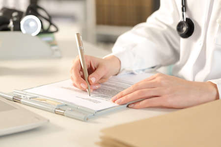 Close up of doctor woman hands filling clinical record sitting on a desk at the office