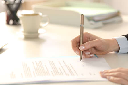 Close up of business woman hand signing contract sitting on a desk in the officeの写真素材