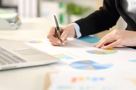 Close up of business woman hands comparing graphs documents on a desk at the officeの写真素材