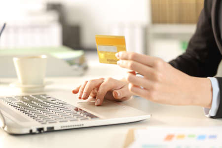 Close up of executive woman hands paying online with credit card on laptop sitting on a desk in the officeの写真素材