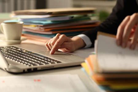 Close up of executive hands working hard late hours using laptop in the night at office checking a pile of documentsの写真素材