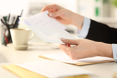 Close up of business woman hand putting letter on an envelope sitting on a desk at the office