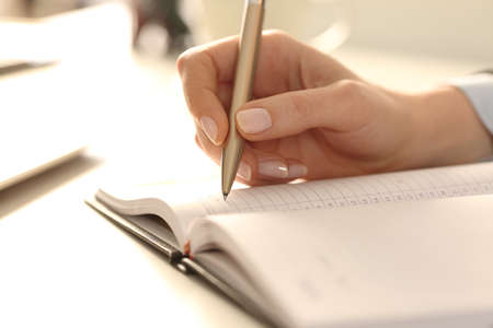 Close up of executive woman hands writing appointment on agenda on a desk in the officeの写真素材