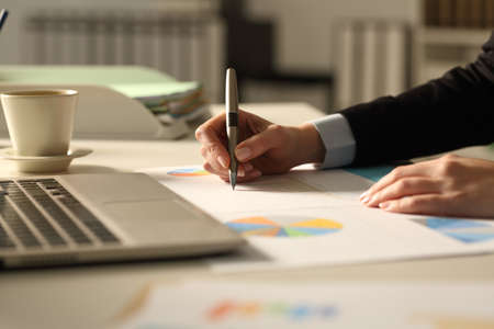 Close up of business woman hands writing on graphs report at night in the officeの写真素材