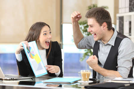 Happy executives celebrating good results with graph report on a desk at the officeの写真素材