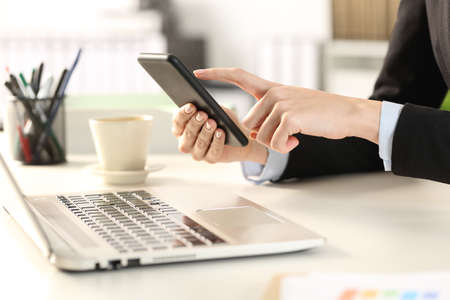 Close up of executive woman hands with laptop checking smart phone at the officeの写真素材