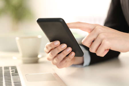 Cloe up of executive woman hands checking smart phone sitting on a desk at officeの写真素材