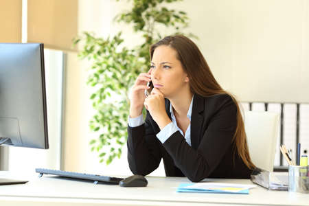 Pensive executive talking on smart phone at office with computerの写真素材