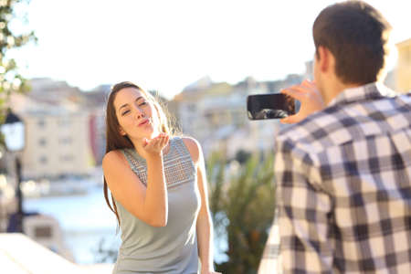 Happy tourists couple taking photos on smart phone on vacation on a beach townの写真素材