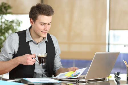 Happy executive man checking growth graph report drinking coffee at officeの写真素材