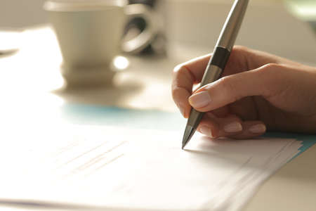 Close up of woman hands signing contract sitting on a desk at night
