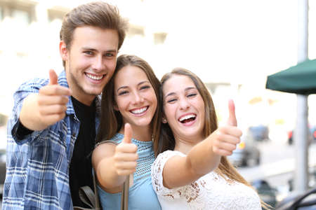 Happy group of three friends with thumbs up and perfect smiles looking camera in the streetの写真素材