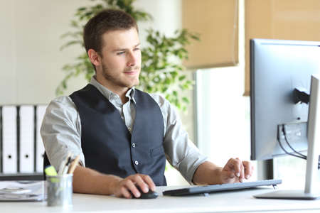 Concentrated executive man using computer sitting on a desk at the officeの写真素材
