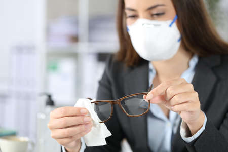 Close up of executive woman hands wearing protective mask disinfecting glasses with sanitizer at the officeの写真素材