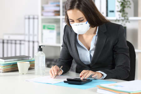 Bookkeeper with protective mask calculating with calculator ticking off document at the officeの写真素材