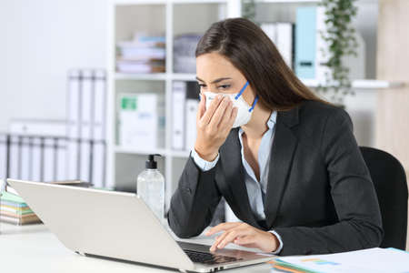 Executive exposing herself to contagion touching protective mask working at officeの写真素材
