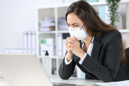 Executive woman wearing protective mask praying with eyes closed on a desk at the officeの写真素材