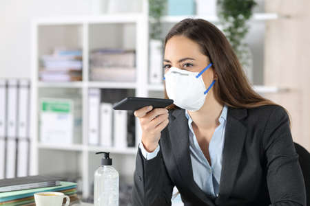 Executive woman with protective mask using voice recognition system on smart phone at the officeの写真素材