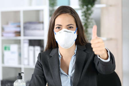Front view of executive woman with protective mask with thumbs up looking camera at the officeの写真素材