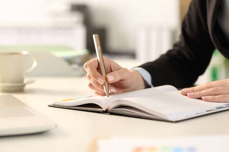Close up of business woman hands taking notes writing on agenda sitting on a desk at the officeの写真素材