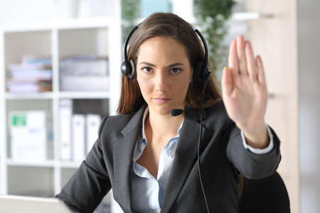 Front view of a serious telemarketer woman with headset gesturing stop sitting at the officeの写真素材