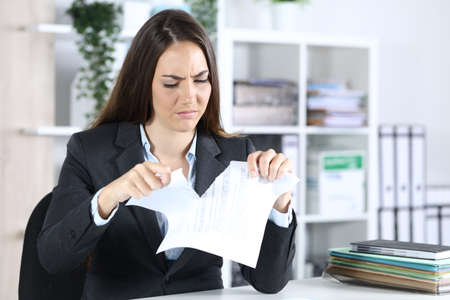 Angry executive woman ripping contract sitting on a desk at the officeの写真素材