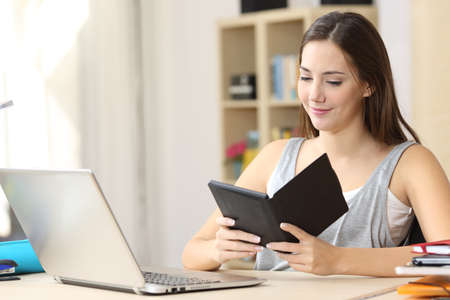 Happy student woman reading ebook on ereader sitting on a desk at homeの写真素材