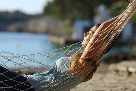 Side view portrait of a relaxed woman sunbathing resting lying on a hammock with arms behind head on the beachの写真素材