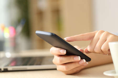 Close up of woman hands using cell phone sitting on a desk at homeの写真素材