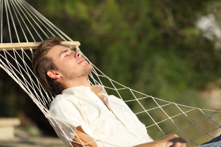 Relaxed man sunbathing resting lying on a hammock with eyes closed outdoors in the mountainの写真素材