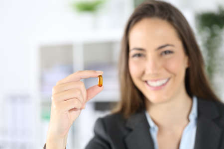Front view of an unfocused happy executive woman showing vitamin pill at officeの写真素材