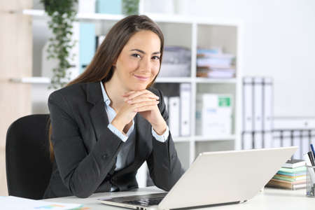 Happy executive woman posing looking at camera sitting on a desk at the officeの写真素材